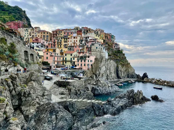 Colorful cliffside houses in Manarola, Cinque Terre, Italy, overlooking serene blue waters and rocky shoreline.