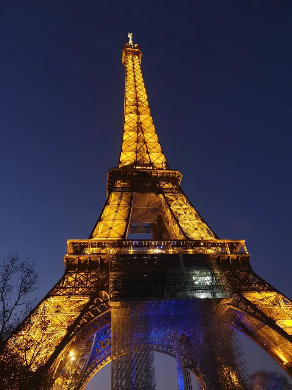 Eiffel Tower illuminated at night in Paris, France, showcasing its iconic architecture against a dark blue sky.